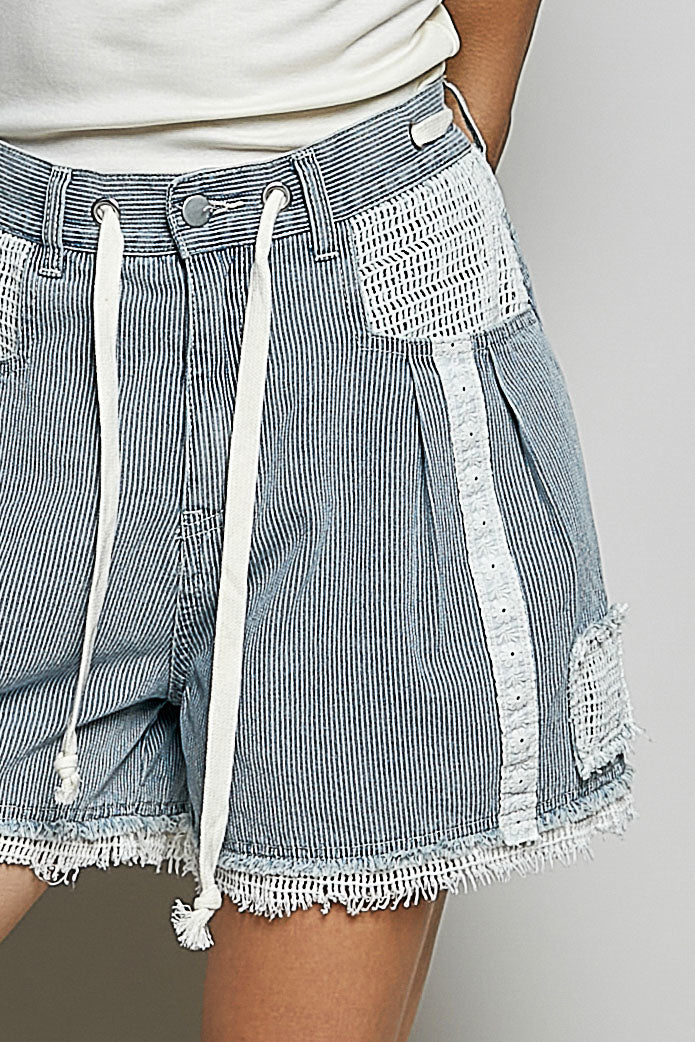 Close-up of blue and white striped shorts with lace detailing on a neutral background
