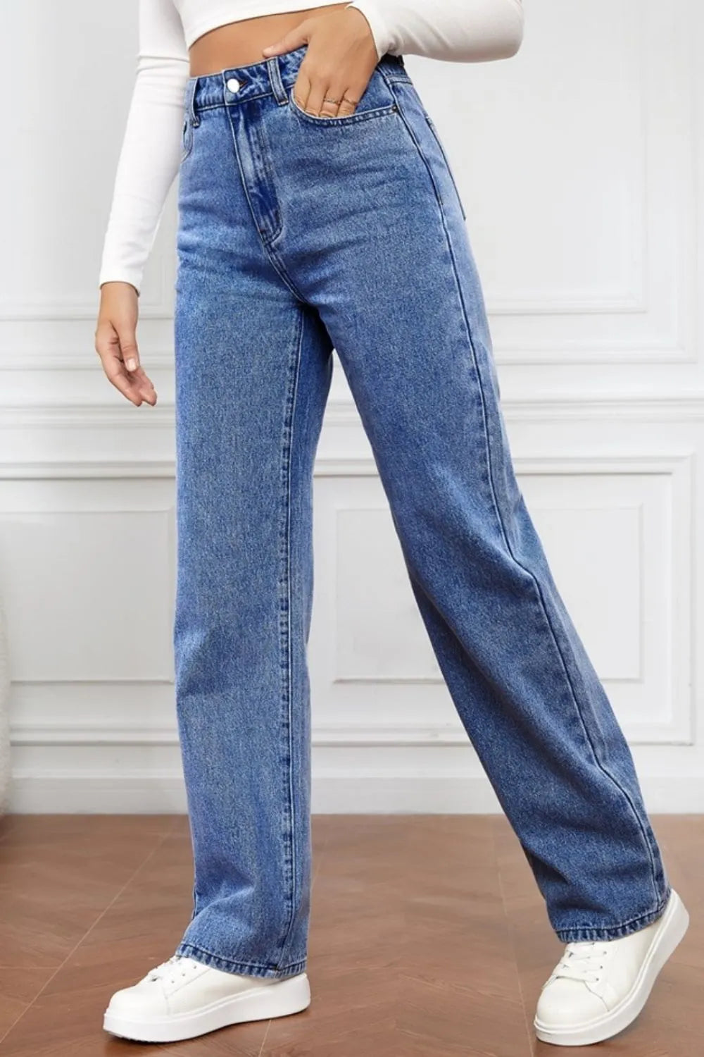 Person wearing blue jeans and white sneakers on a plain background
