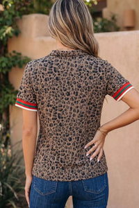 Person wearing a leopard print shirt with red and green trim, standing against a beige wall.