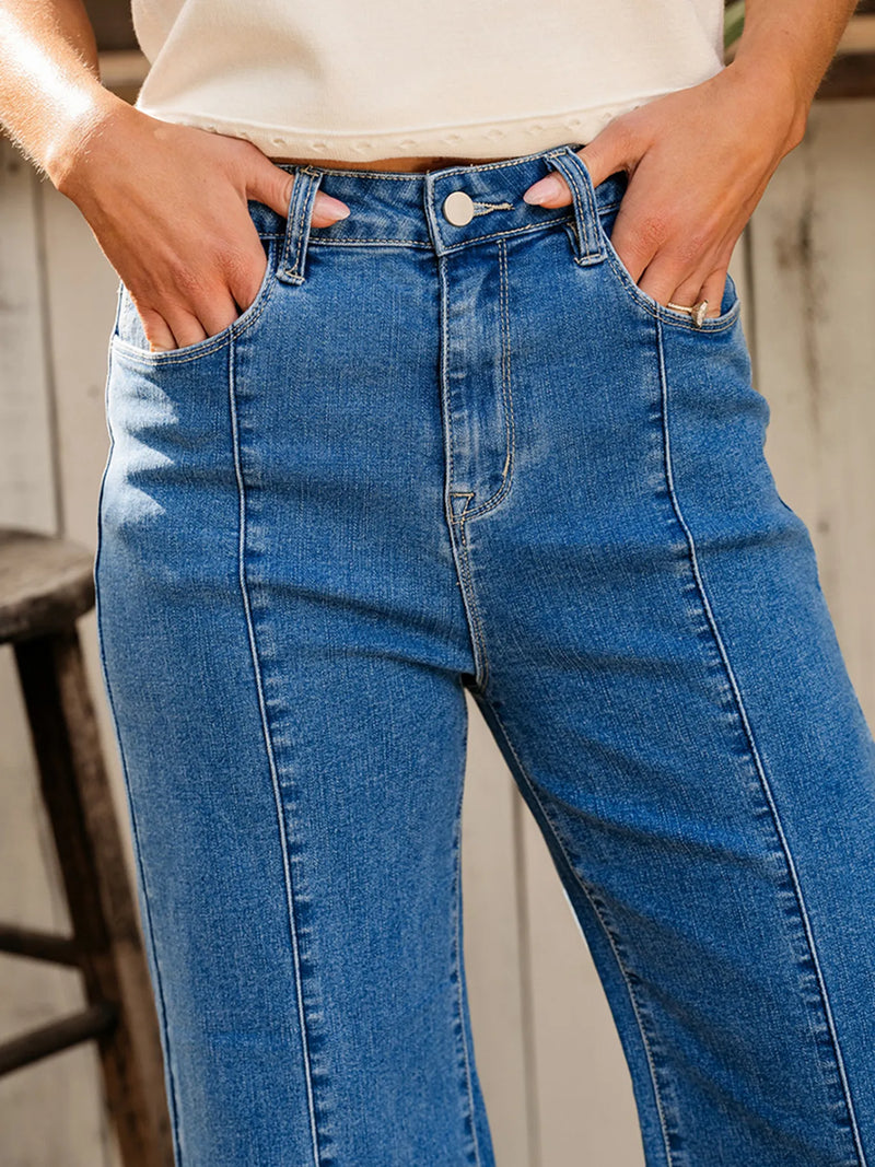 Person wearing blue jeans with hands in pockets against a neutral background