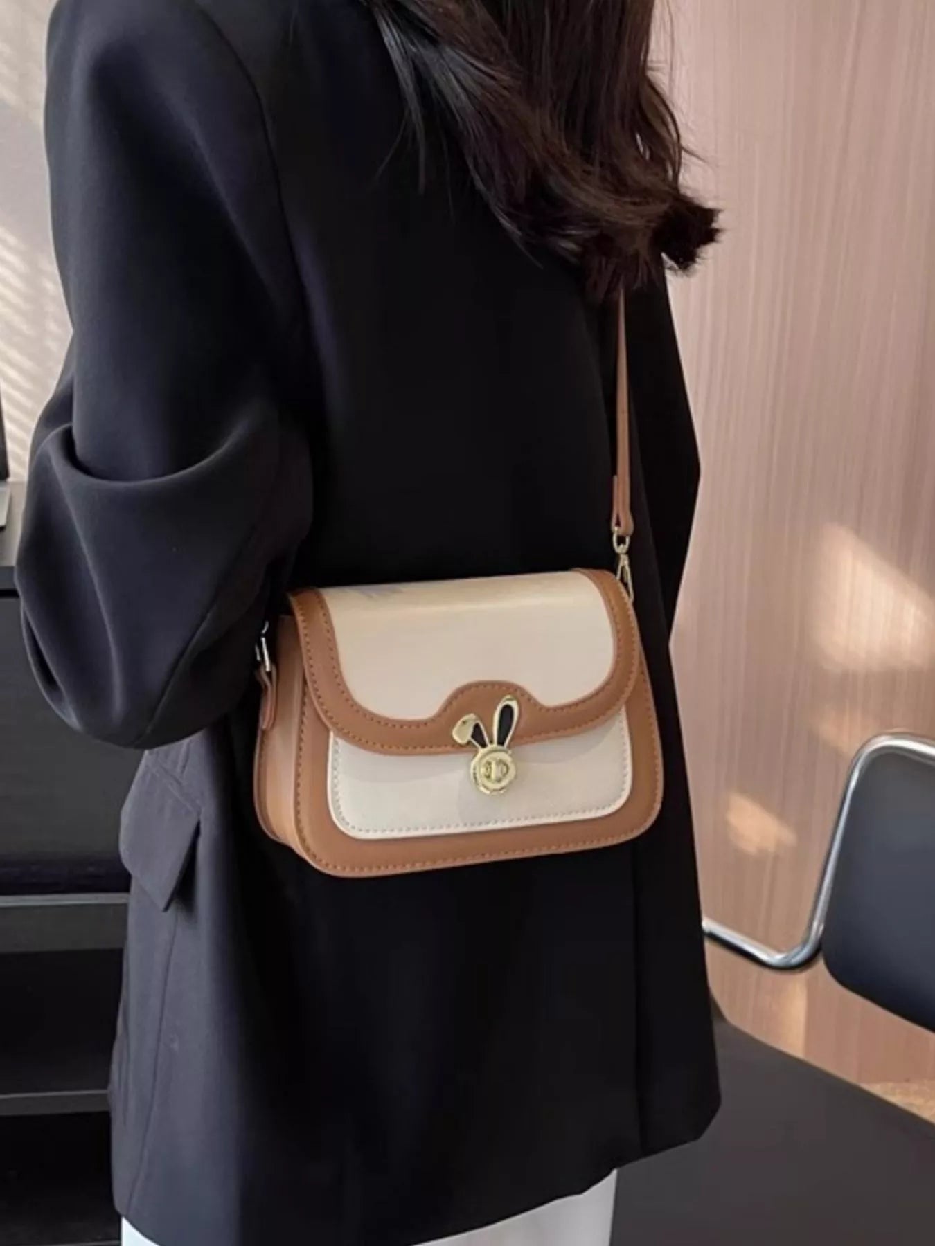 Person wearing a black coat with a beige and brown handbag.