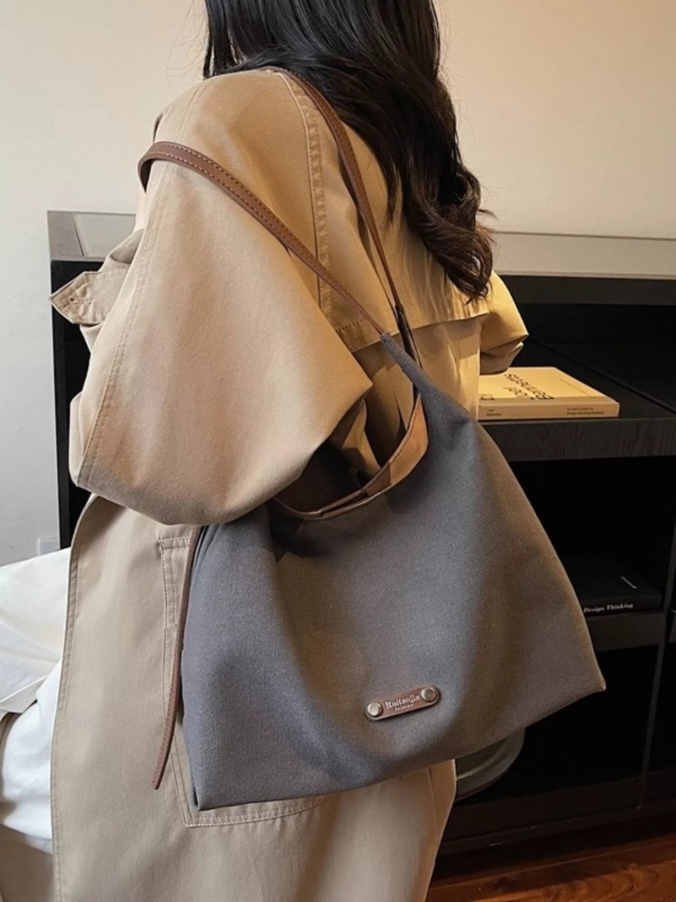 Person wearing a beige jacket with a gray shoulder bag indoors.