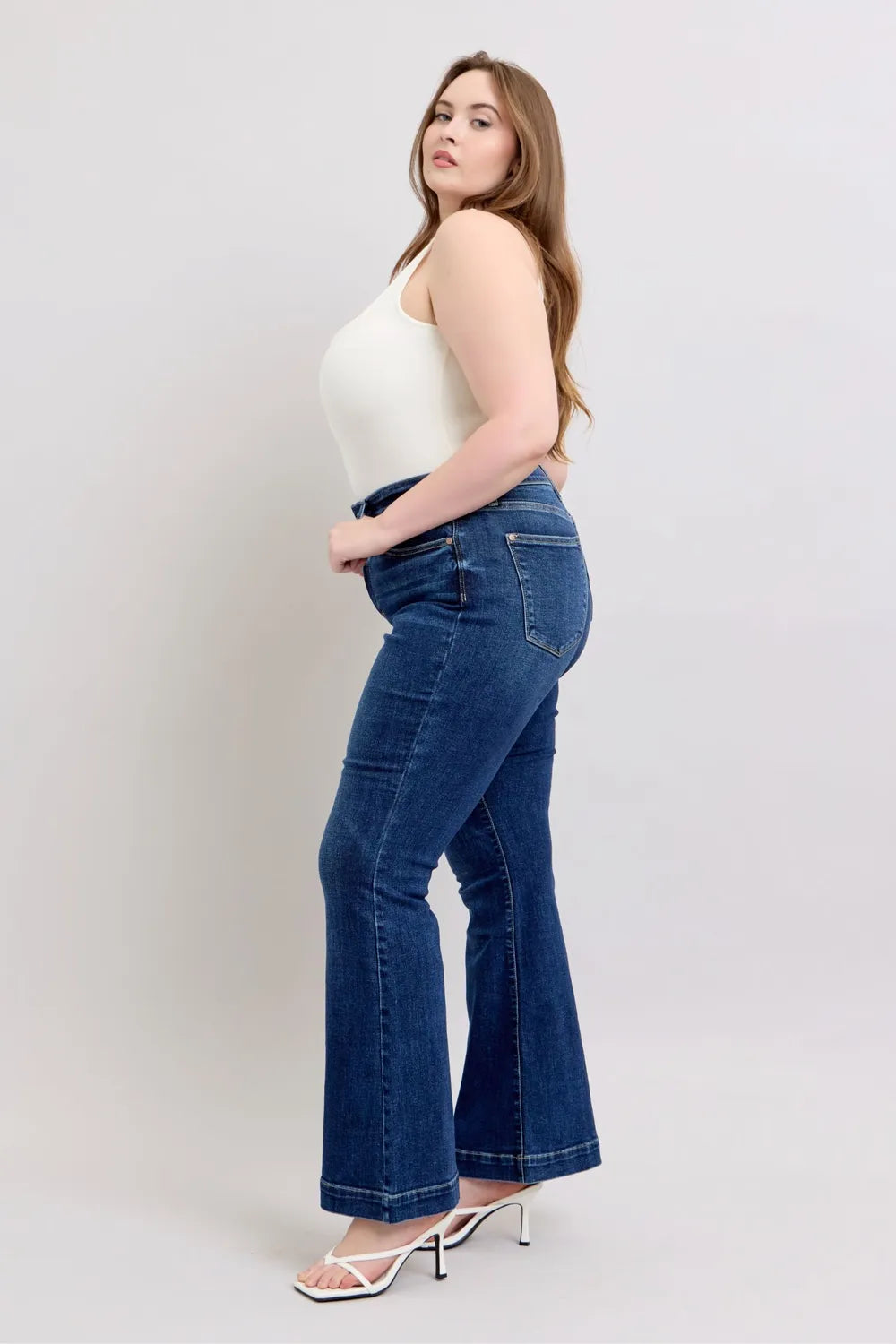 Woman wearing blue jeans and a white top on a plain background