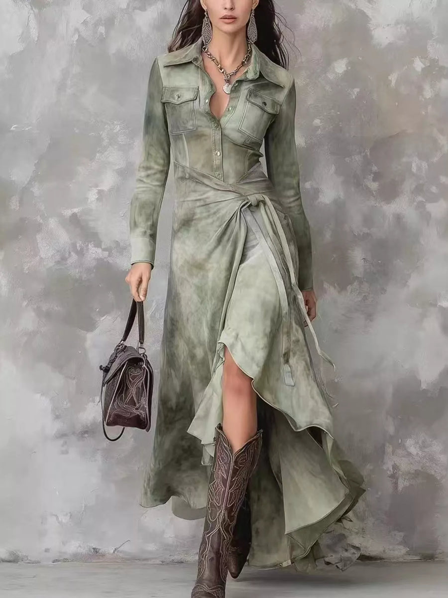 Woman wearing a long green dress with a high-low hemline and holding a brown handbag against a textured gray background.