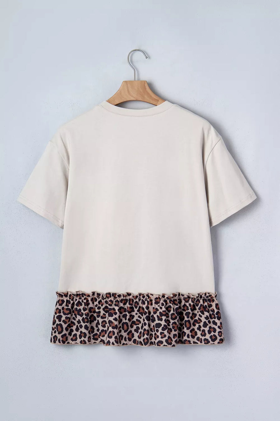 Beige t-shirt with leopard print hem on a hanger against a light gray background