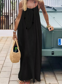 Woman in a black dress holding a woven bag on a tiled pavement.