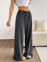 Person wearing gray wide-leg pants in a room with a couch and pillows.