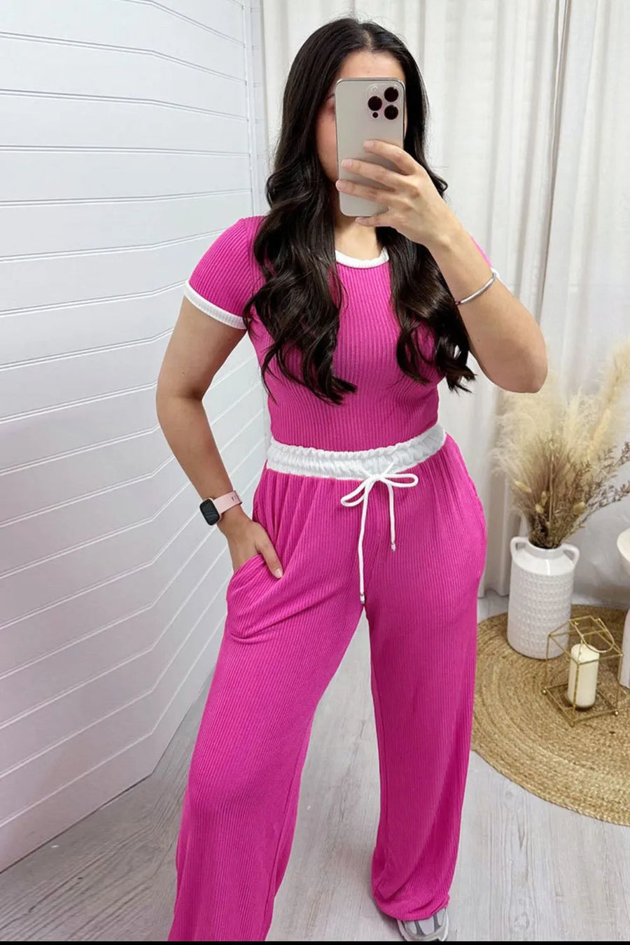 Woman taking a mirror selfie wearing a pink outfit with white accents.