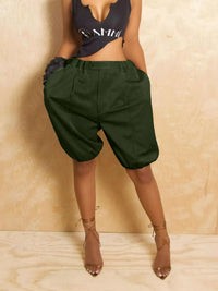 Person wearing green harem shorts and a black crop top against a beige background