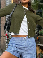 Person wearing a green cardigan, white shirt, and blue shorts with a black bag.
