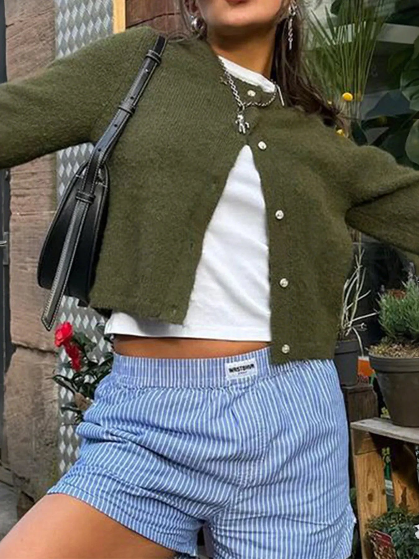 Person wearing a green cardigan, white shirt, and blue shorts with a black bag.