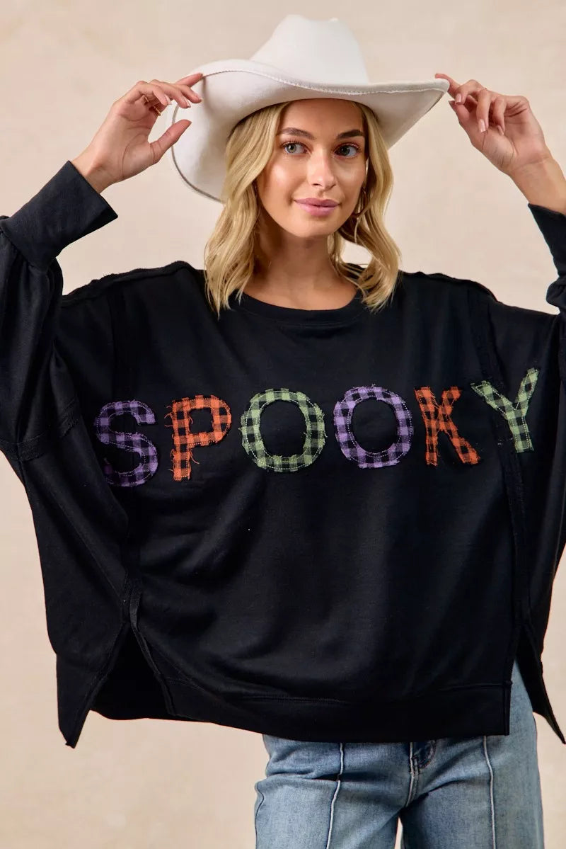 Woman wearing a black sweatshirt with colorful 'SPooky' text and a white cowboy hat.