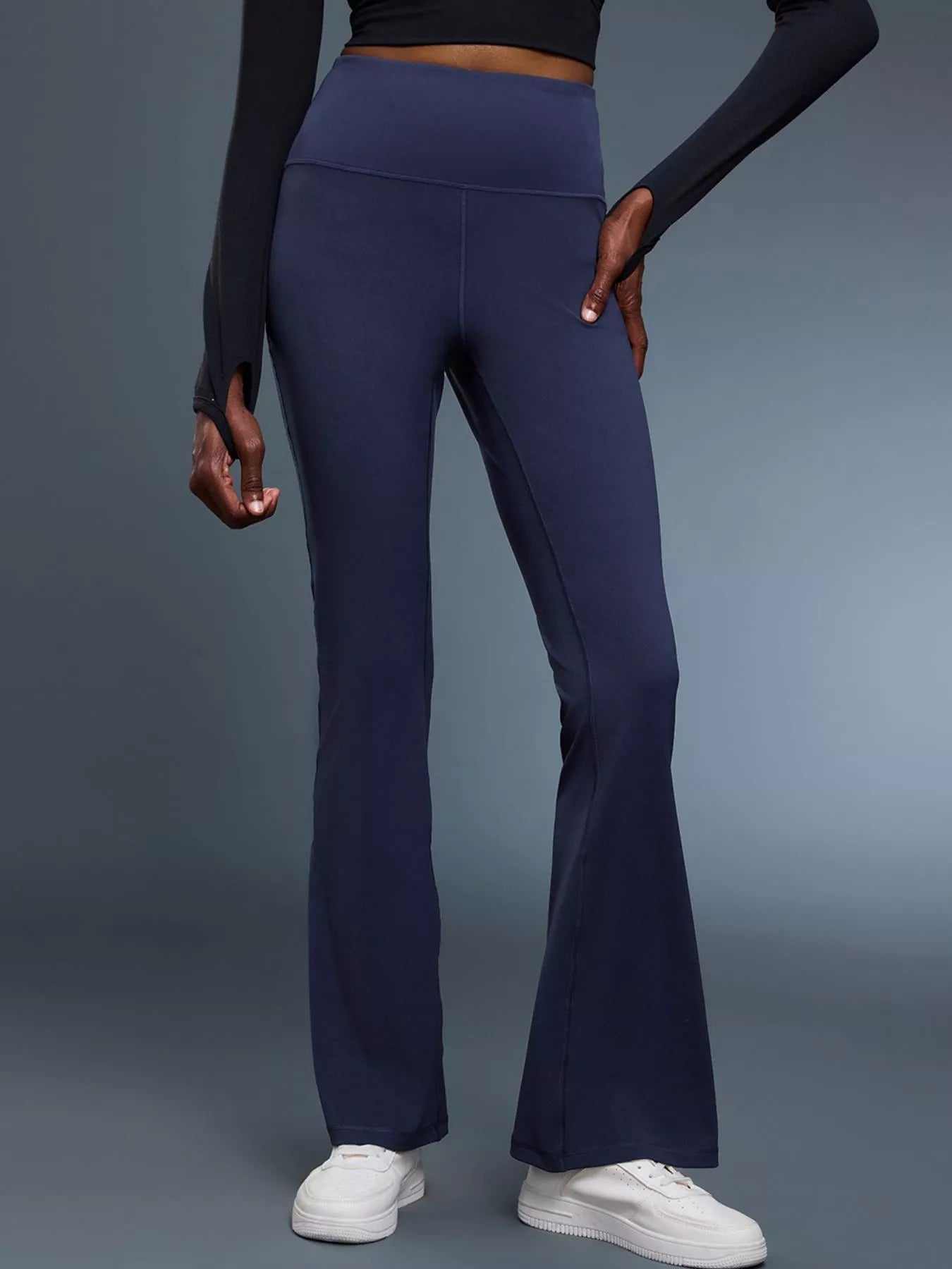 Person wearing navy flared pants and white sneakers on a gray background