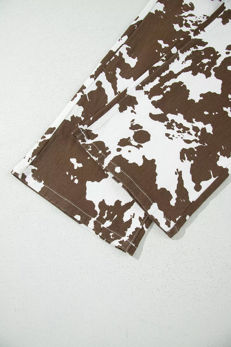 A close-up of a folded garment or fabric piece featuring a brown and white cow-print pattern, laid flat on a light gray textured surface.