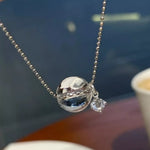 Silver necklace with a spherical pendant and small diamond on a blurred background