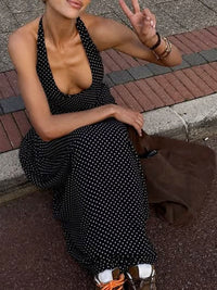 Woman in a black polka dot dress sitting on a sidewalk, making a peace sign.
