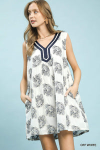 Woman wearing a white dress with black floral pattern and blue neckline against a light blue background