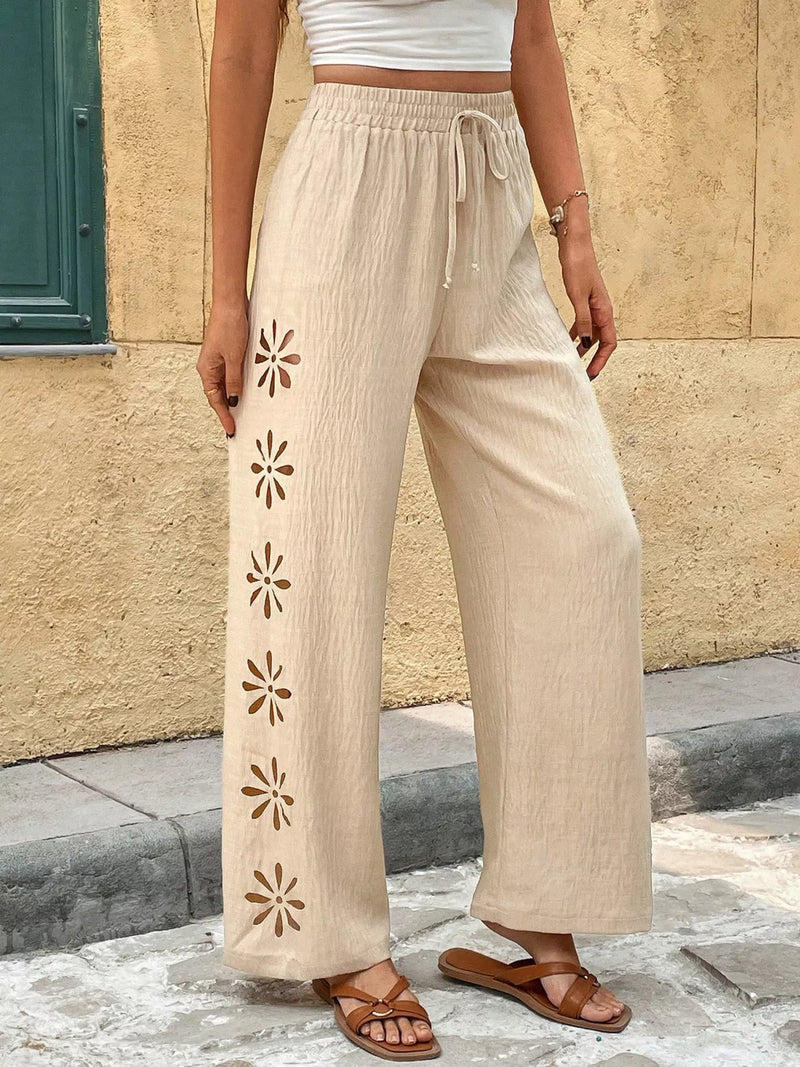 Person wearing beige pants with floral cut-out sides against a stone wall.