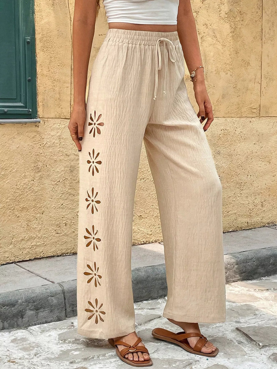 Person wearing beige pants with floral cut-out sides against a stone wall.