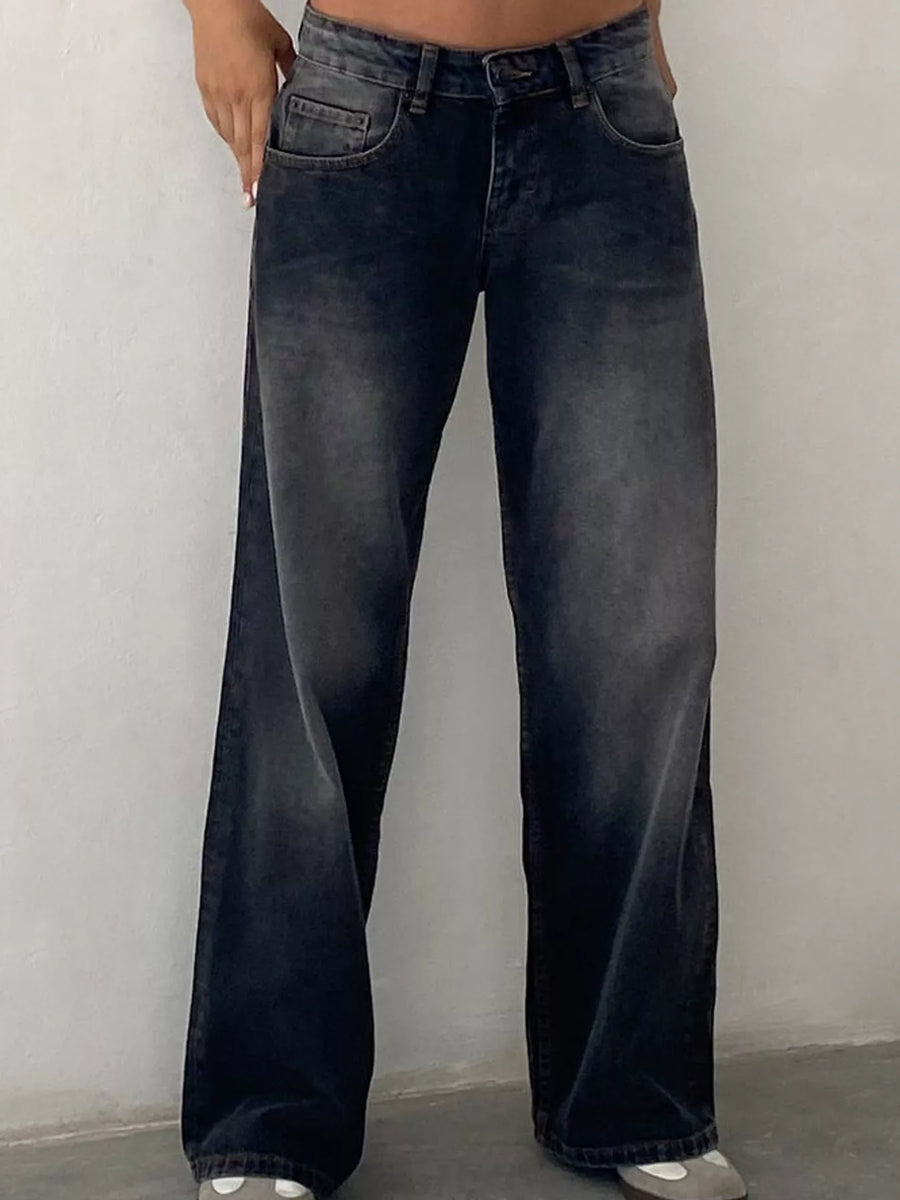 A person wearing dark gray to black wide-leg jeans with a faded wash, shown from the waist down against a plain light gray wall.