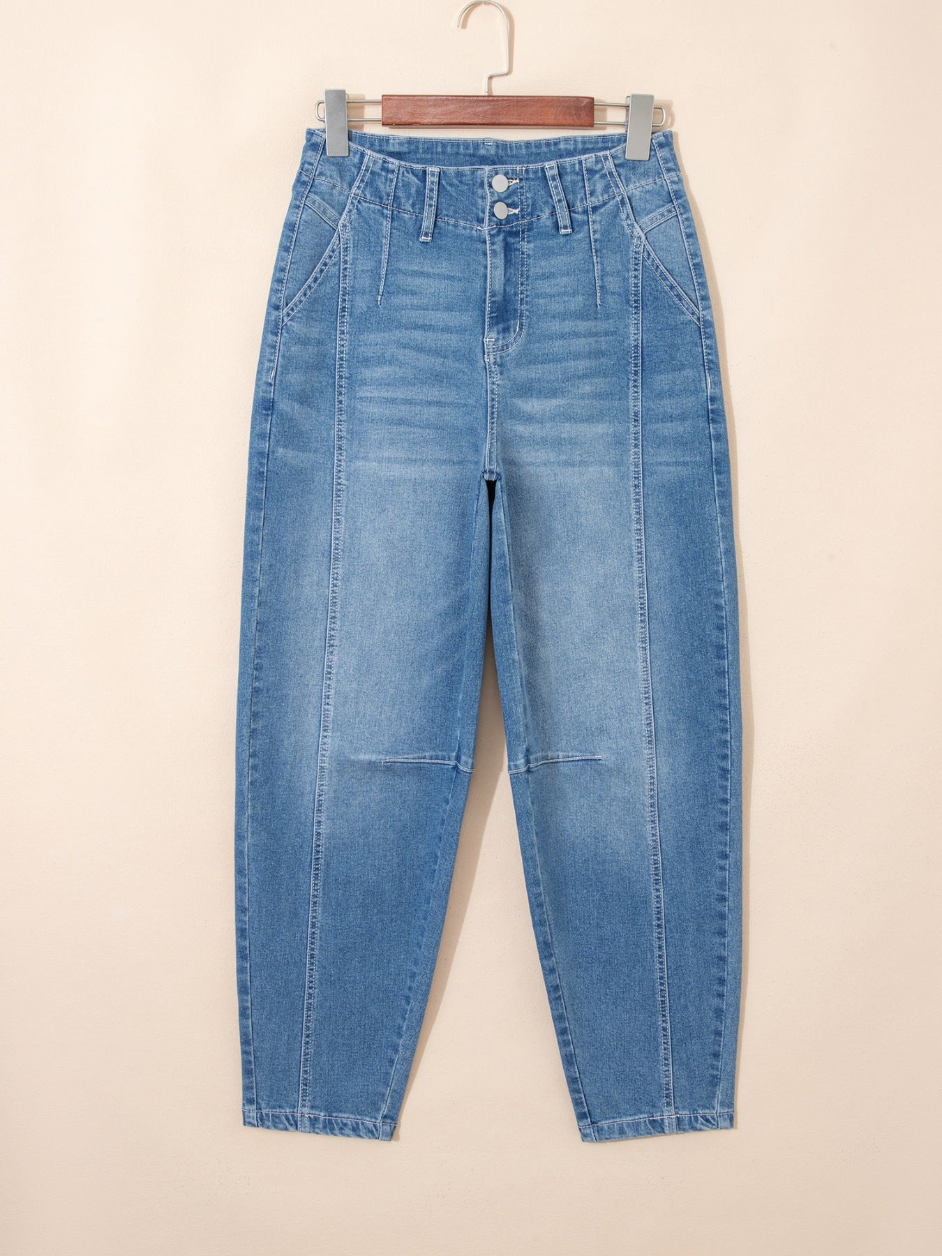 Blue jeans hanging on a wooden hanger against a beige background