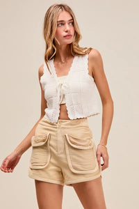 Woman wearing a white sleeveless top and beige shorts on a beige background
