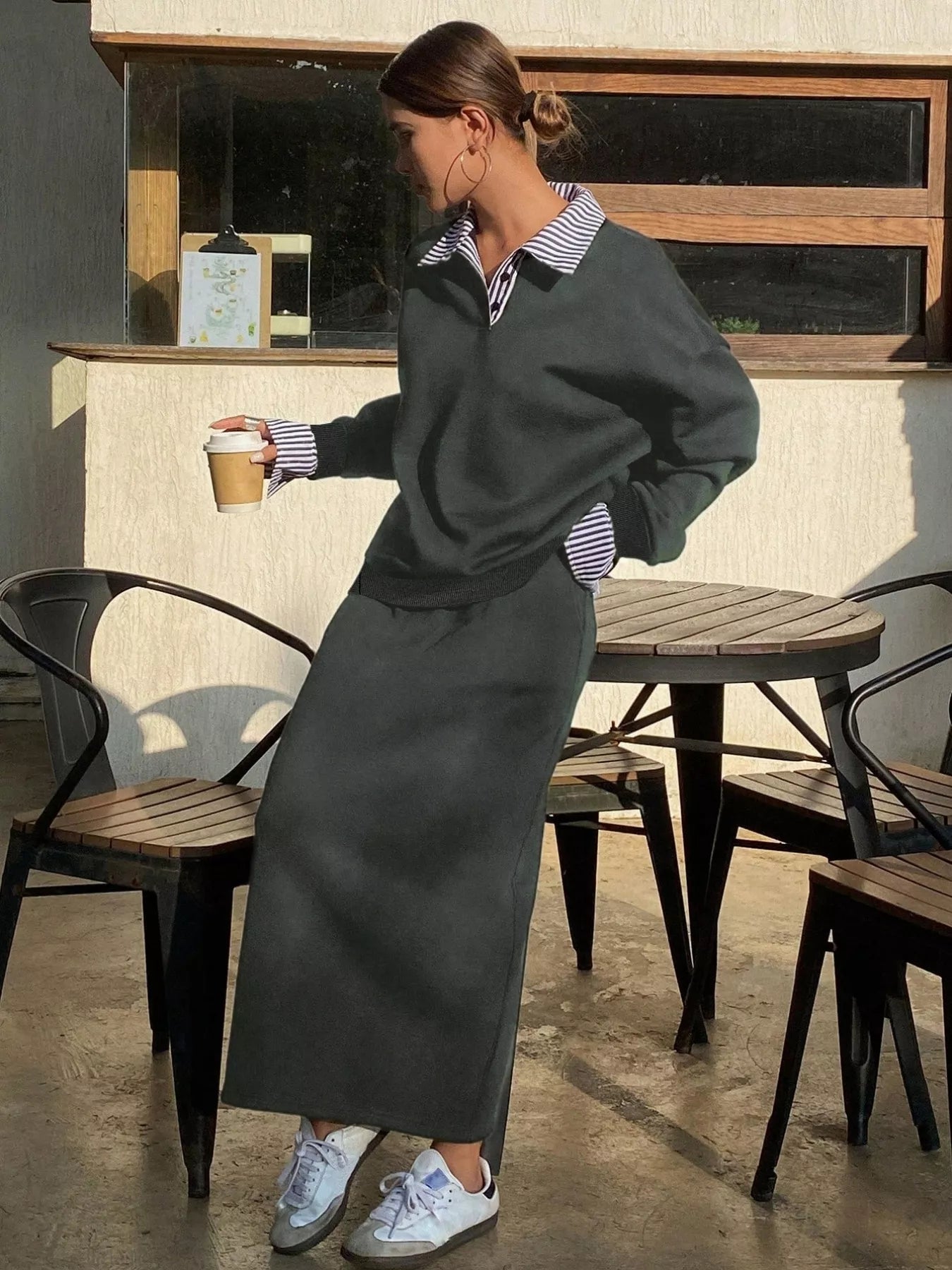 Woman in a gray outfit holding a coffee cup in an outdoor setting.