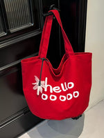 Red tote bag with 'hellooooo' text and flower design hanging on a door handle.
