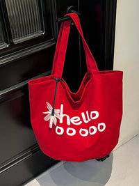 Red tote bag with 'hellooooo' text and flower design hanging on a door handle.