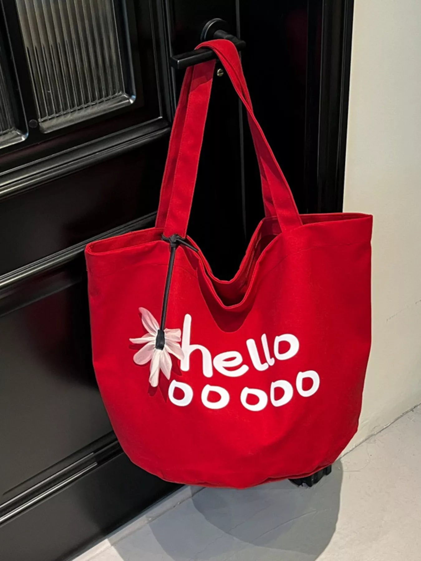 Red tote bag with 'hellooooo' text and flower design hanging on a door handle.