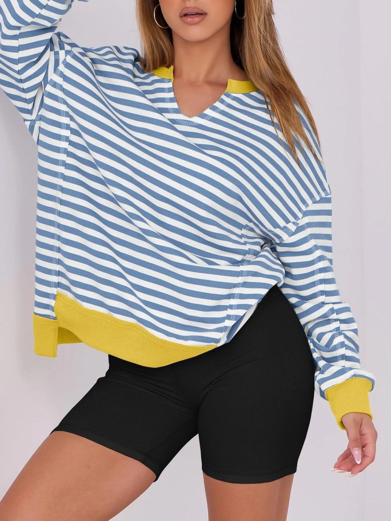 Woman wearing a blue and white striped long-sleeve top with yellow accents and black shorts on a plain background