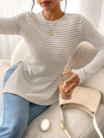 Person wearing a light gray sweater holding a drink with a straw on a couch.