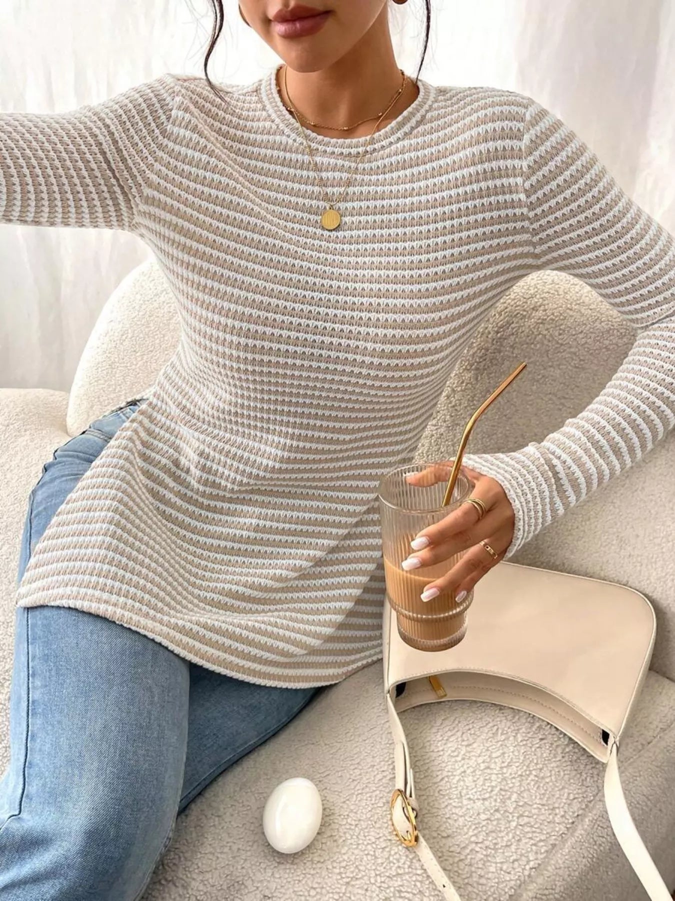 Person wearing a light gray sweater holding a drink with a straw on a couch.