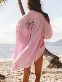 Person wearing a pink cover-up with a palm tree design on a beach.