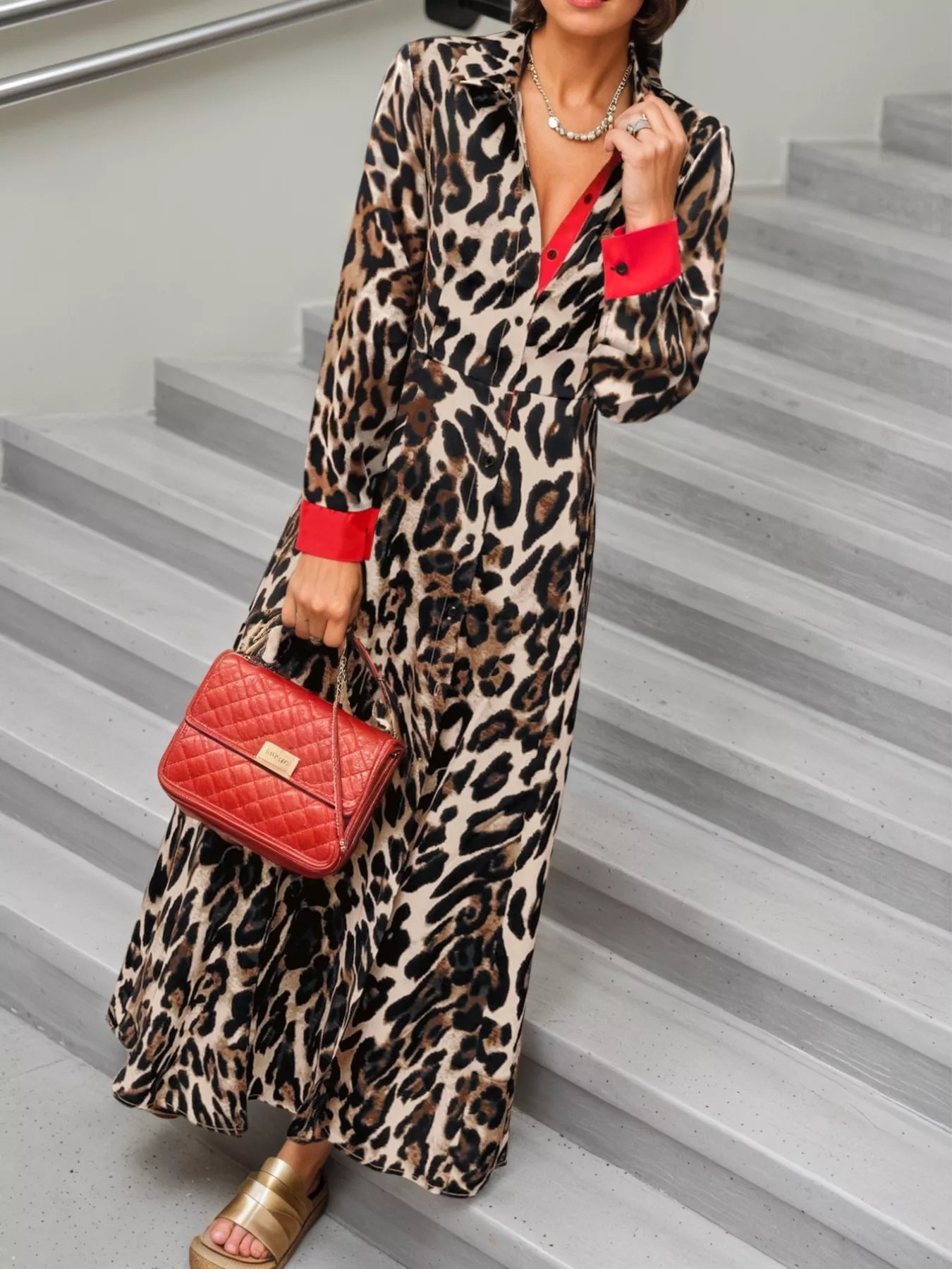Person wearing a leopard print dress with red accents and holding a red handbag on stairs.