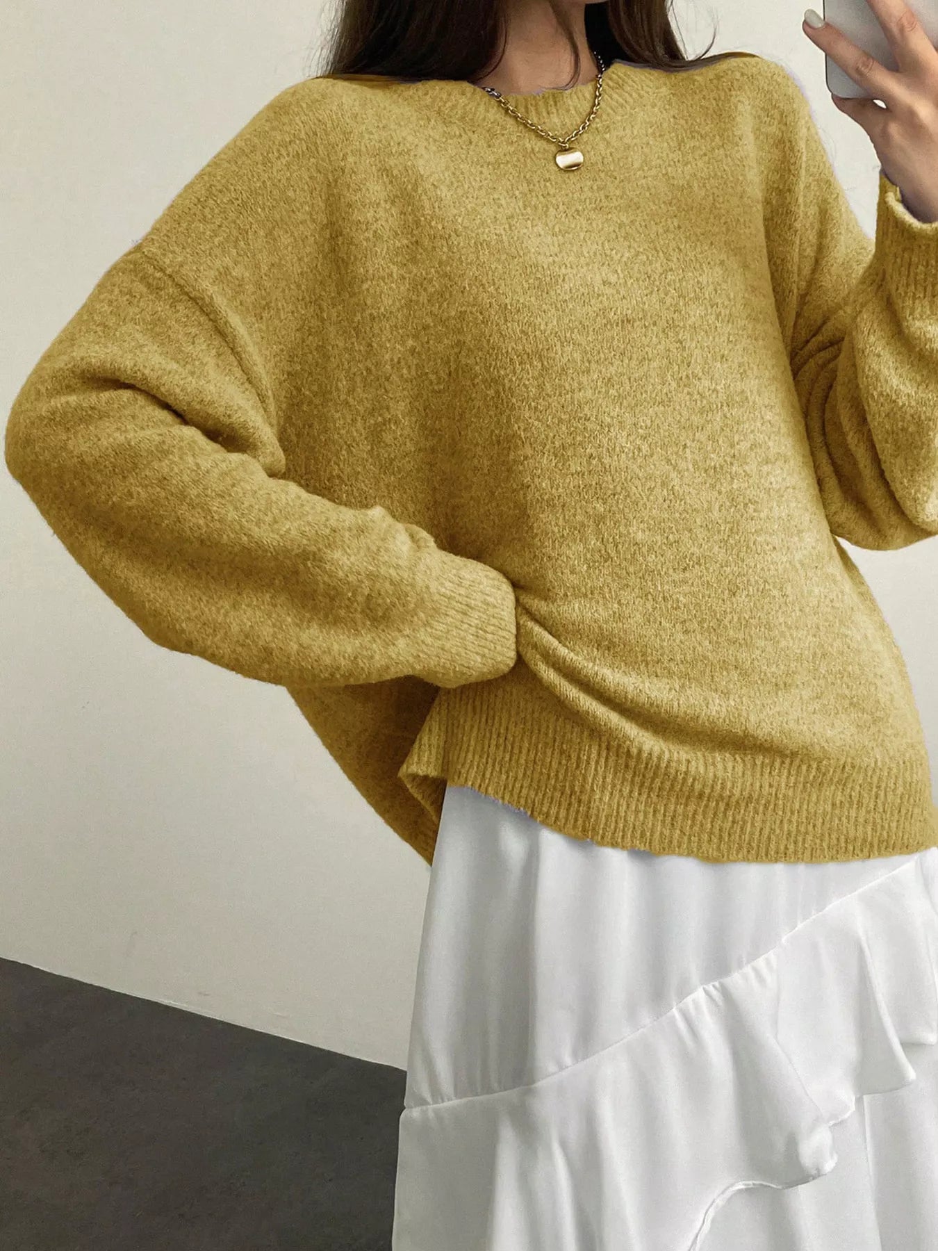 Person wearing a mustard yellow sweater and white pants against a neutral background