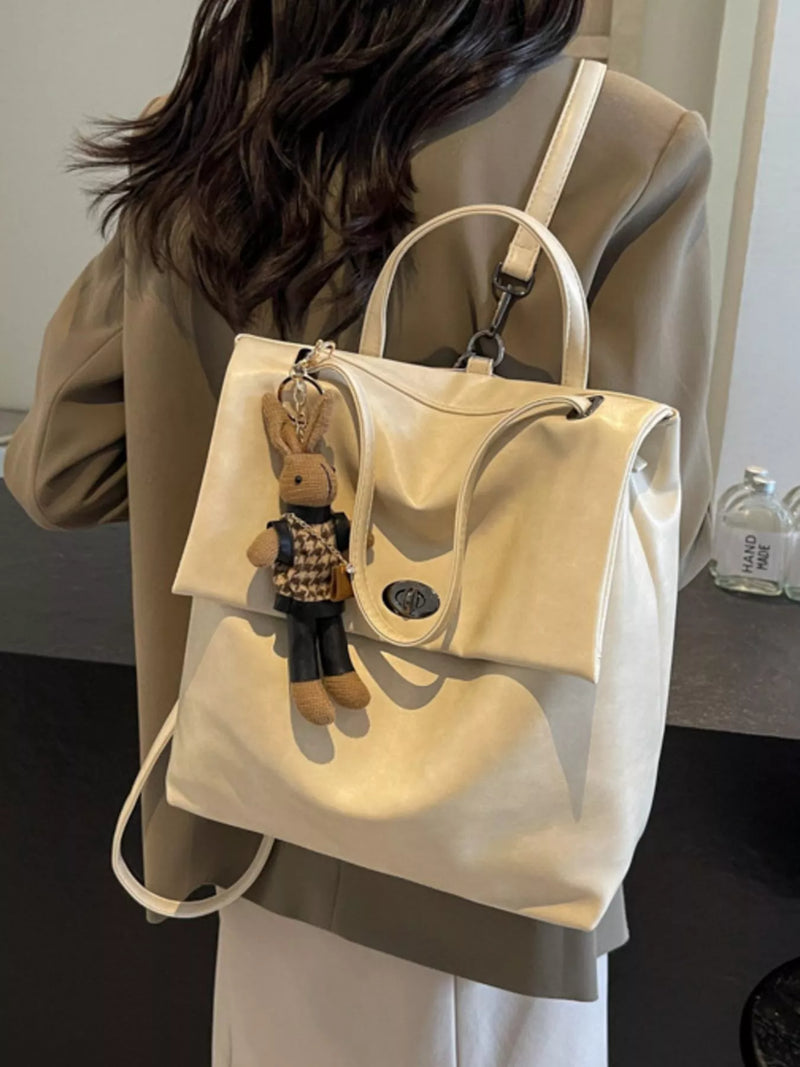 White handbag with a teddy bear keychain worn by a person indoors.