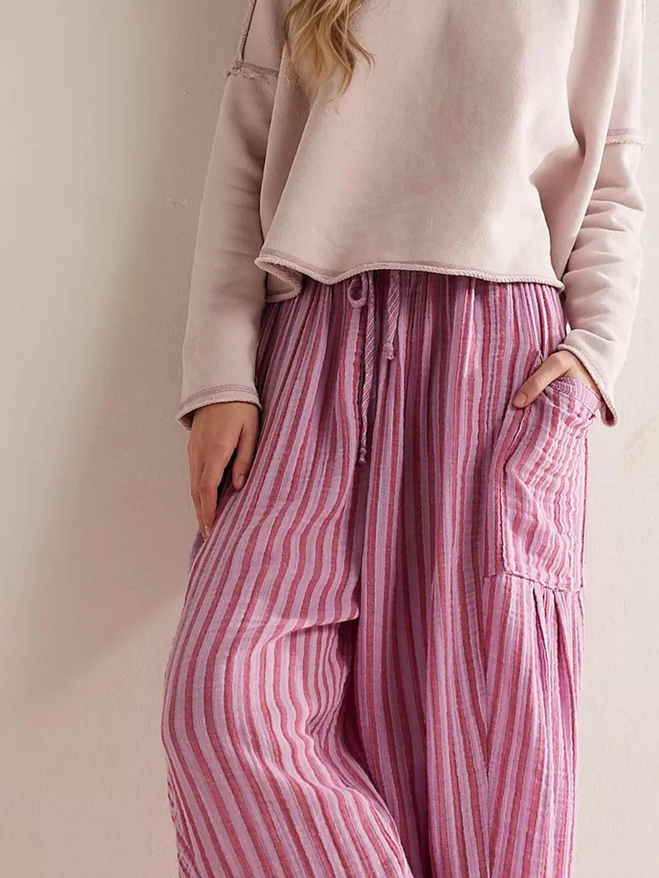 Person wearing a light pink cropped hoodie and pink striped pants against a neutral background