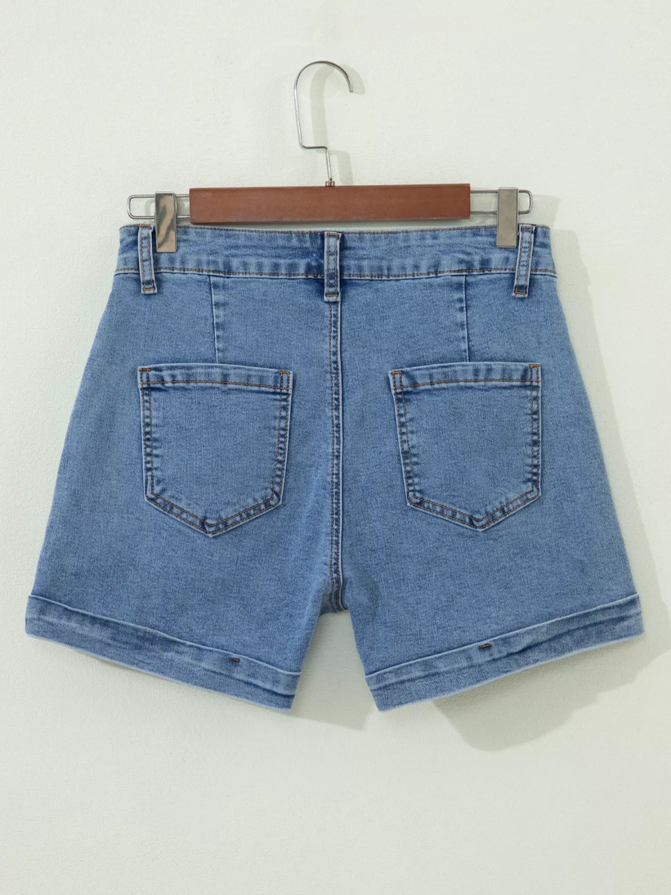 Blue denim shorts on a hanger against a white background