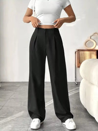 Person wearing black wide-leg pants and a white top in a minimalistic room.