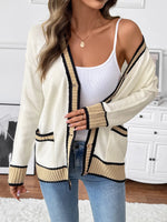 Woman wearing a cream cardigan with black trim, white top, and blue jeans indoors.