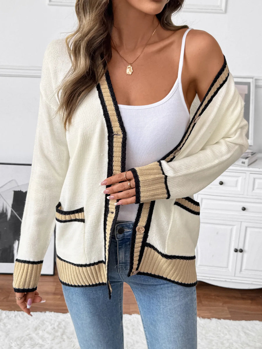 Woman wearing a cream cardigan with black trim, white top, and blue jeans indoors.