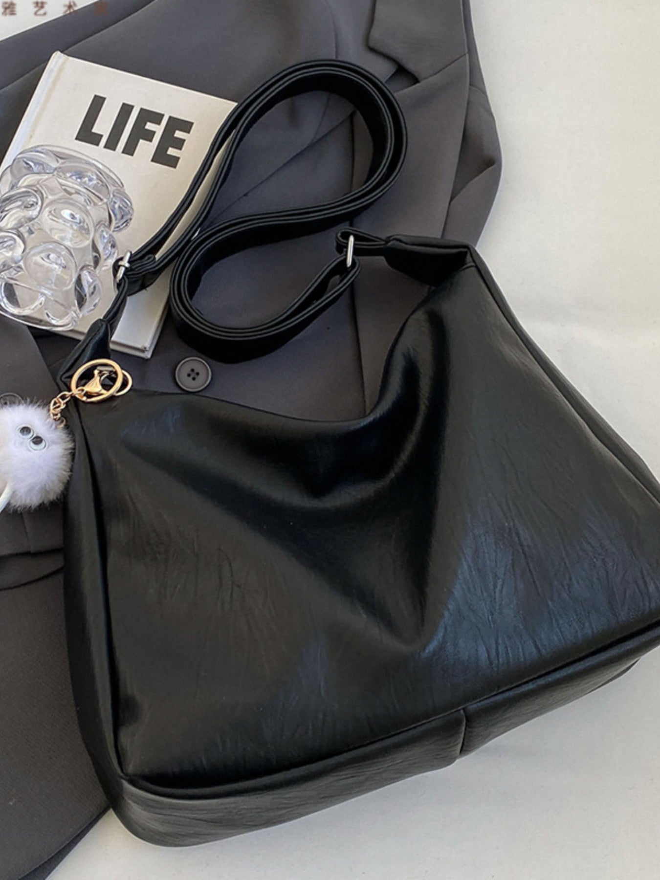 Black handbag with a 'LIFE' magazine and clear glass on a white surface