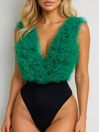 Woman wearing a green feathered top and black swimsuit against a white background