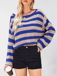 Person wearing a blue and beige striped sweater with black shorts on a white background