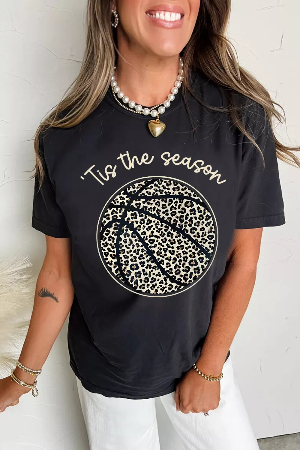 Person wearing a black t-shirt with 'Tis the season' and leopard print design.