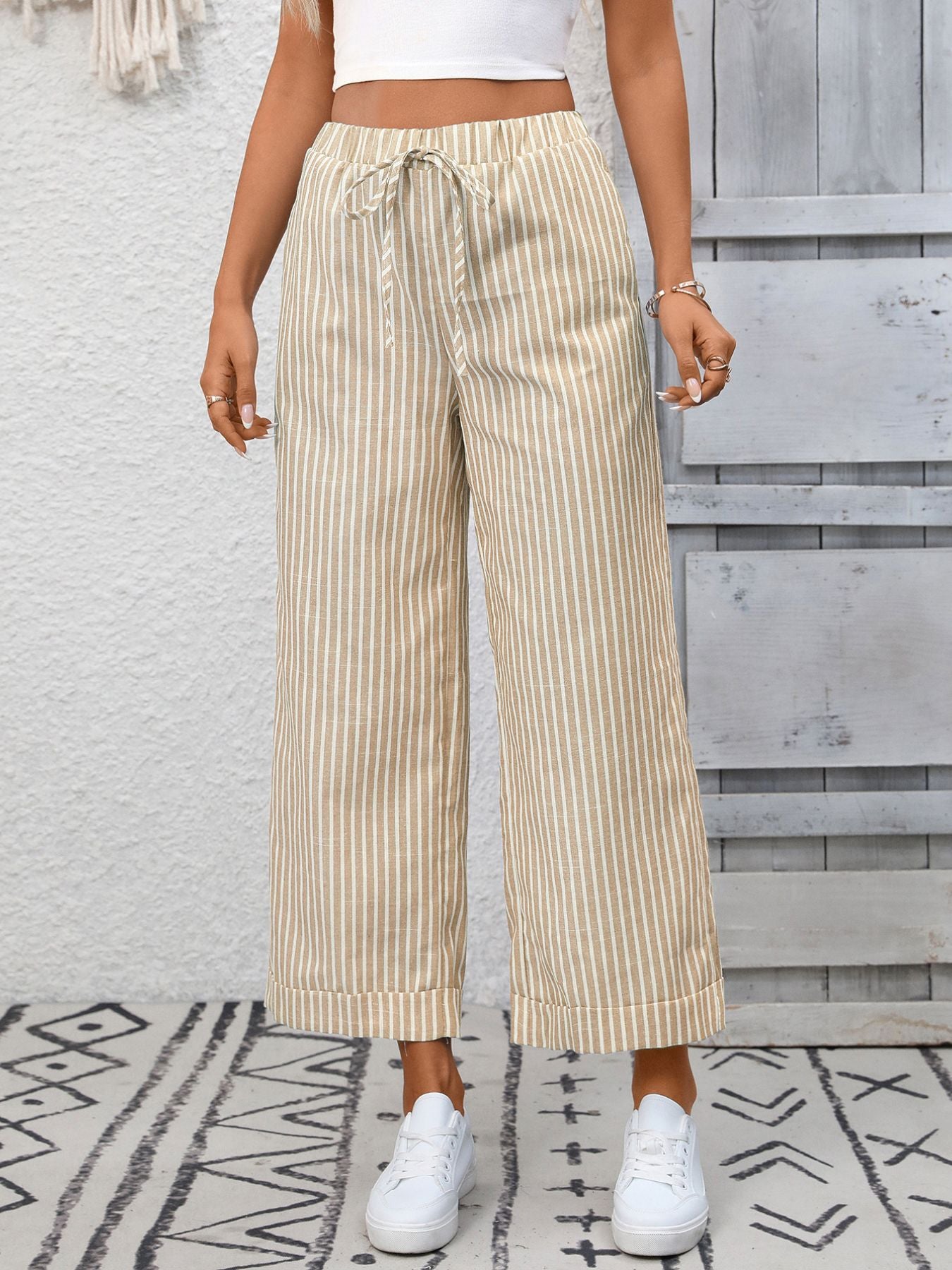 Person wearing beige striped pants with a white top and white sneakers in front of a wooden wall.