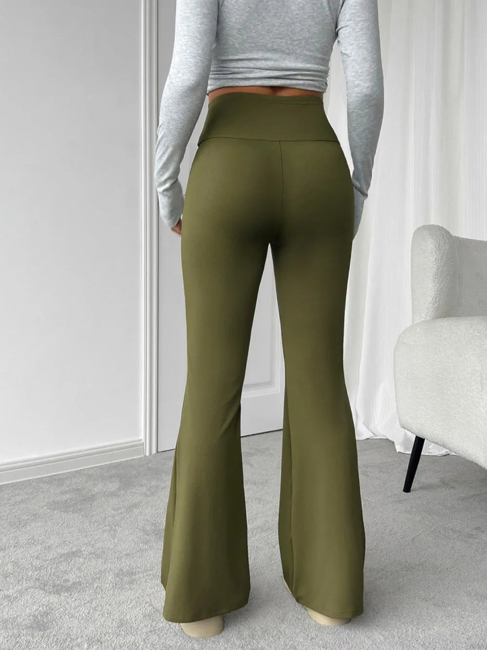 Person wearing olive green flared pants and a gray long-sleeve top in a minimalistic room.