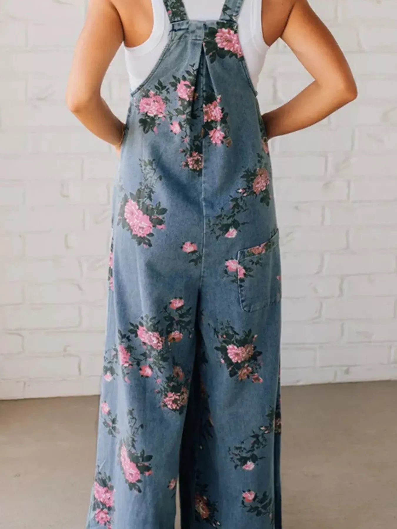 Person wearing floral denim overalls against a white brick wall.