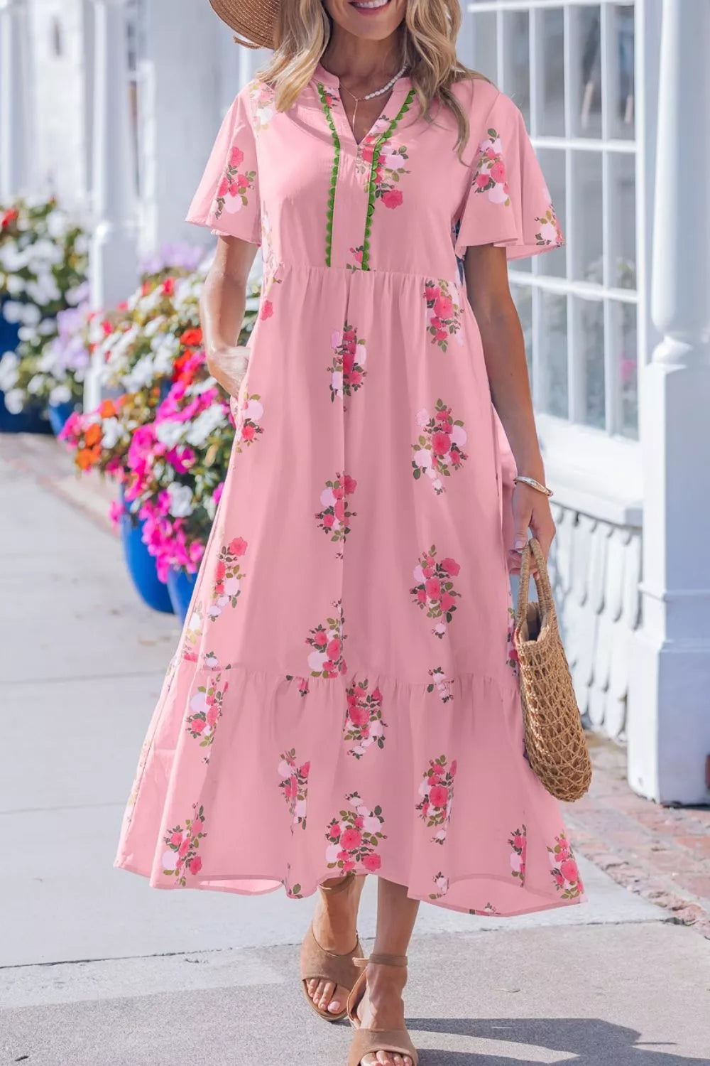 Woman wearing a pink floral dress standing in front of a white building with flowers.
